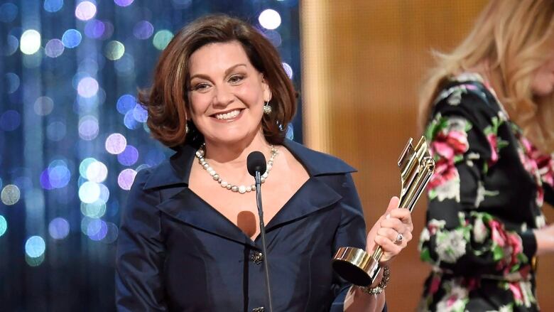 A woman smiles while holding an award on stage. 