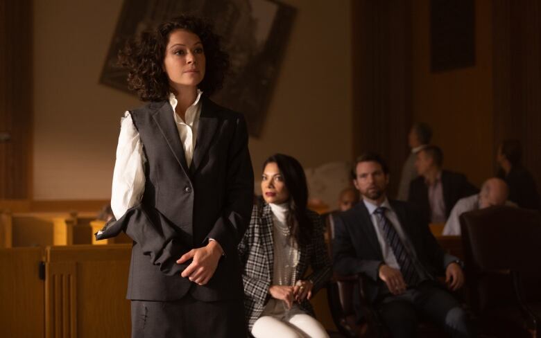 A lawyer stands in a courtroom, with one sleeve of her jacket torn off.  