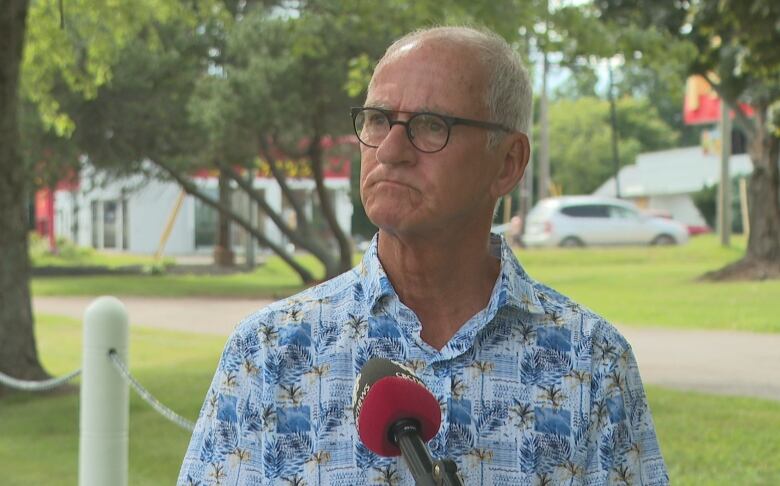 Man in a patterned shirt looks off camera against a green grass background. 