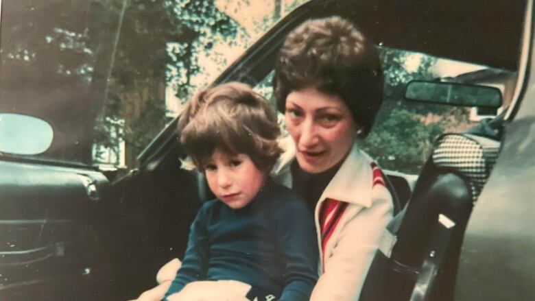 A brown-haired woman holding her young son on her lap while fixing his shoe lace.