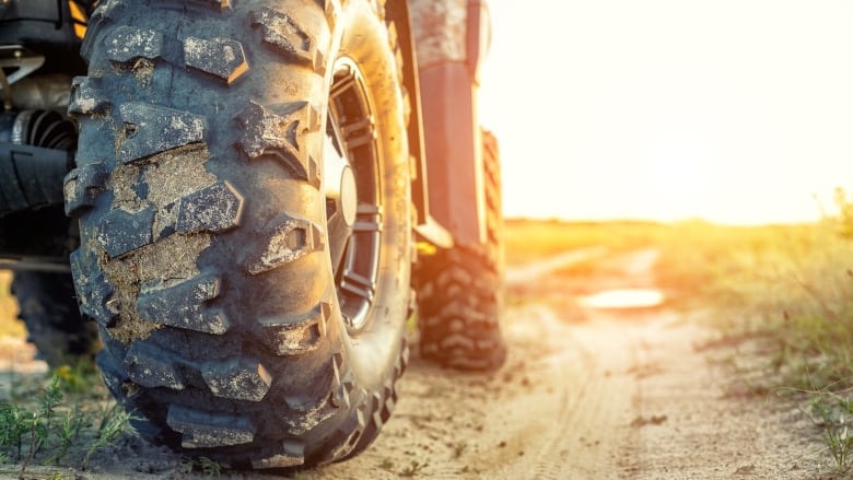 A stock image shows a closeup of the tires of an all-terrain vehicle on a dirt road, with the setting sun in the background.