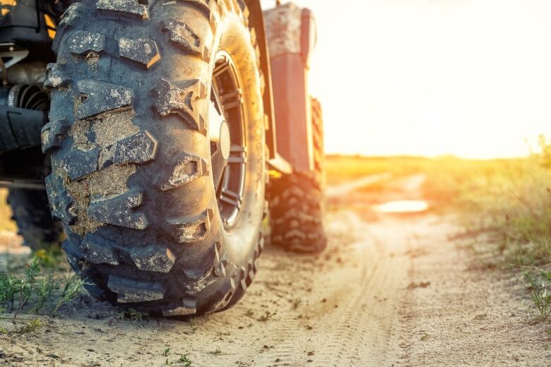 A stock image shows a closeup of the tires of an all-terrain vehicle on a dirt road, with the setting sun in the background.