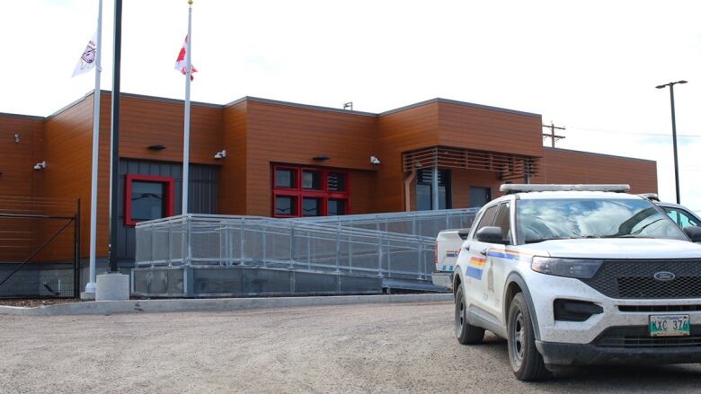 A police vehicle sits in a parking lot in front of a building with a brown wooden exterior.