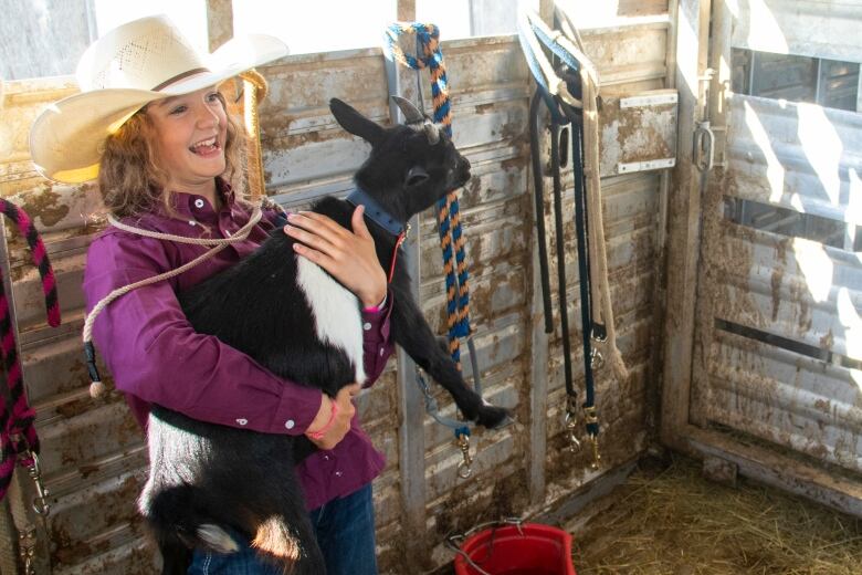 A young girl wearing a cowboy hat holds a goat.