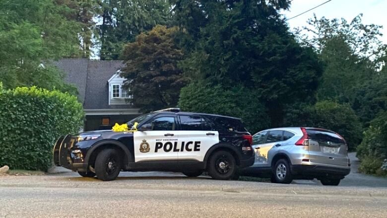 Two police cars are seen outside hedges at a mansion.