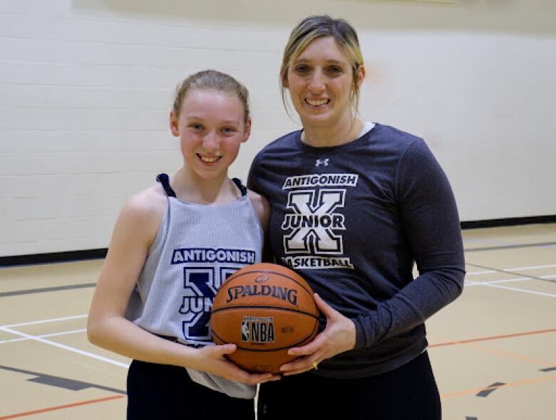 A woman and a girl stand on a basketball court holding a basketball.