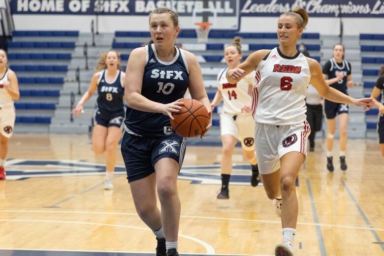 A woman runs down the basketball court with a ball in her hands as another runs behind her.