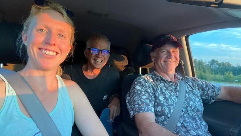 A woman and two men smile in the cab of a truck.