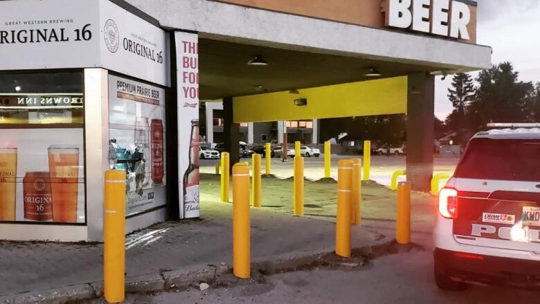 A police car is parked outside a beer store. The window of the store is broken.