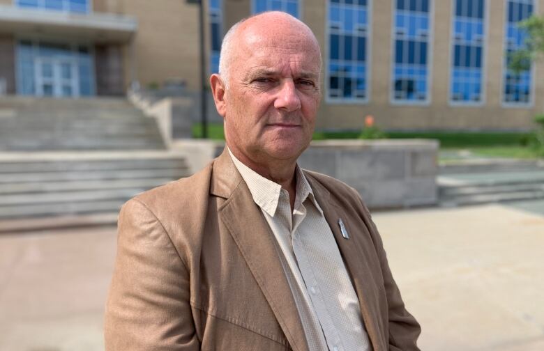 A person wearing a tan blazer stands in front of the Confederation Building in St. John's.