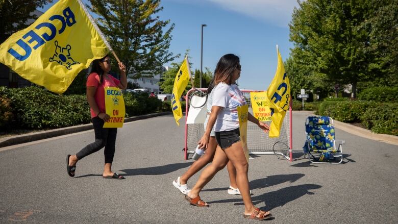 People waving yellow BCGEU flags walk on the road