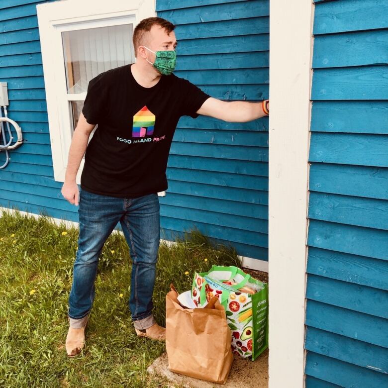 A man wearing a mask knocks on a house door to deliver groceries.