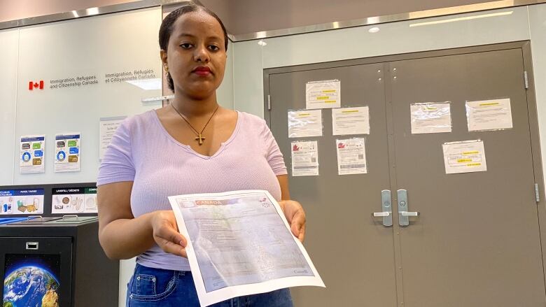 A woman stands in front of the government's immigration office, holding a piece of document.