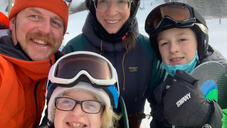 Family smiling, wearing ski goggles and hats. 