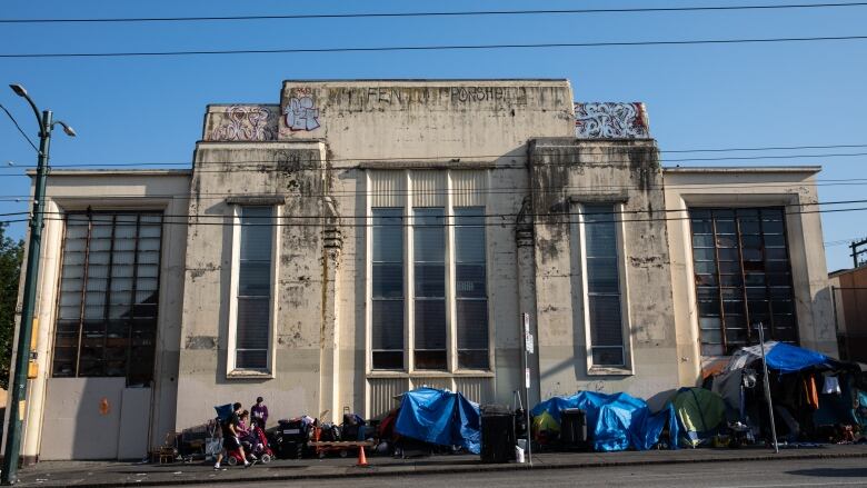 A series of tents lie along a pavement in front of a square building.