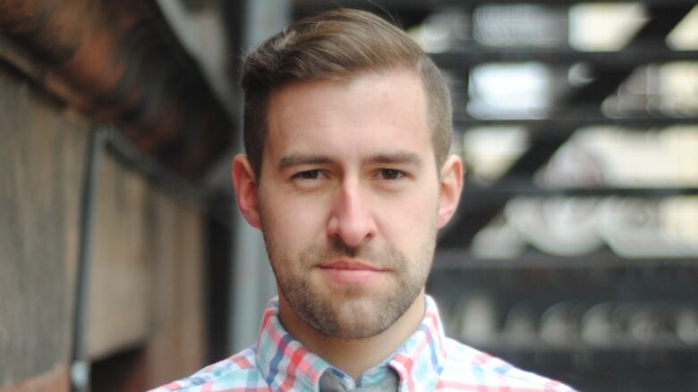 A man's face, up close, almost smiling. He is wearing a collared shirt.