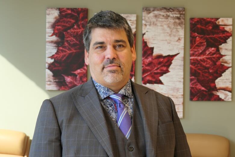 A man in a suit stands in an office, with artwork showing a red maple leaf behind him.