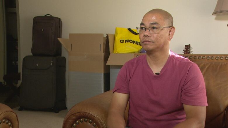 A man wears glasses with a neutral expression while sitting in a living room.