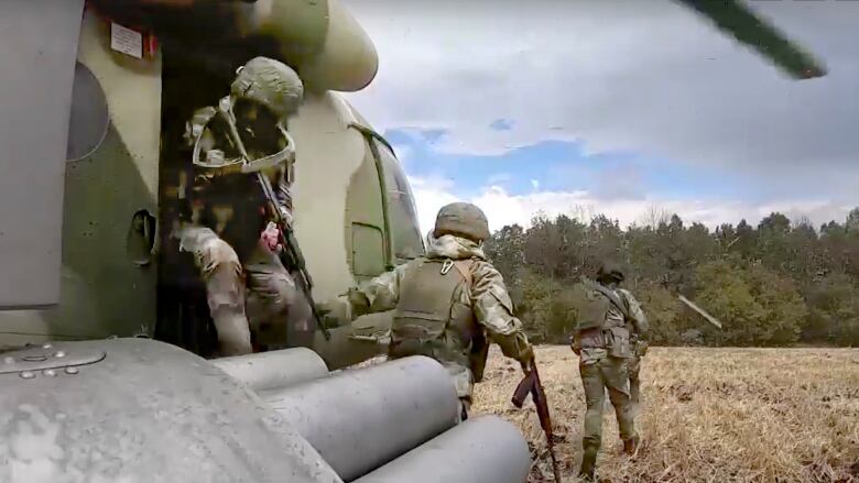 Three uniformed soldiers exit a helicopter on a field. 