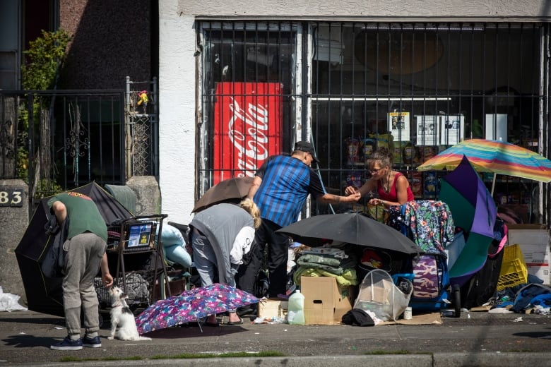 Three people huddle around tents on a sidewalk.