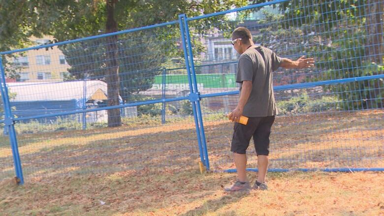 Blue fencing around a grassy area, with a man pictured touching the fences.