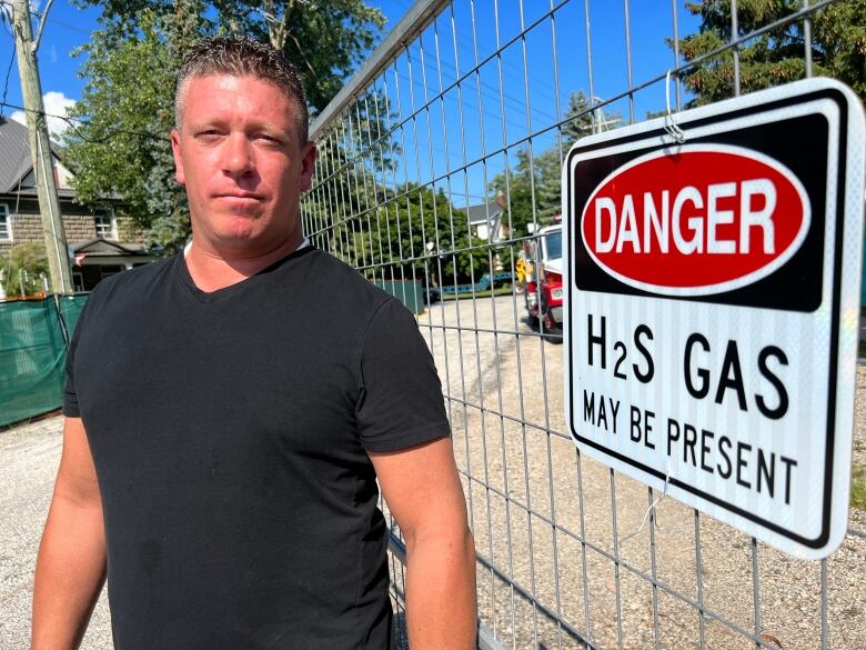 Paul De Goey stands beside an H2S gas is present sign