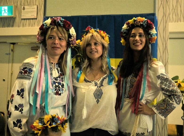 Three women wear traditional Ukrainian clothing while posing for a photograph together 