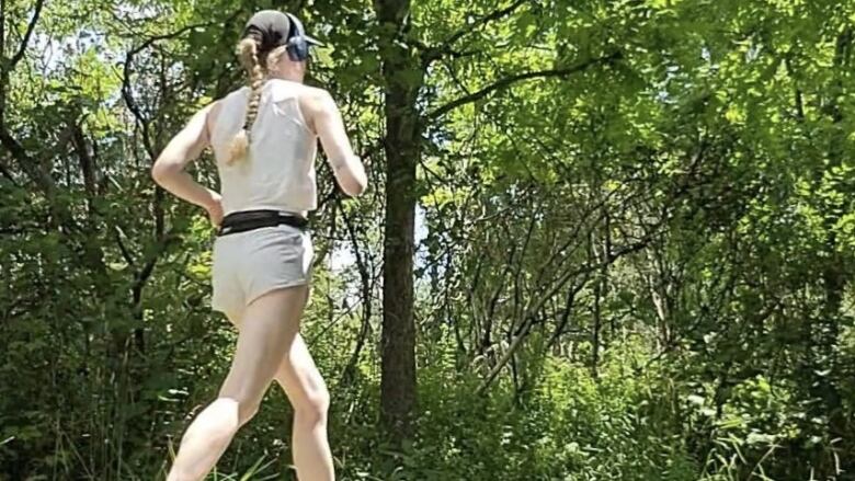 A blonde woman wearing headphones runs on a sunny day. 