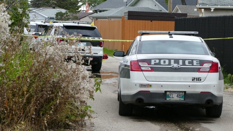 The back of two police vehicles parked behind yellow crime scene tape. 