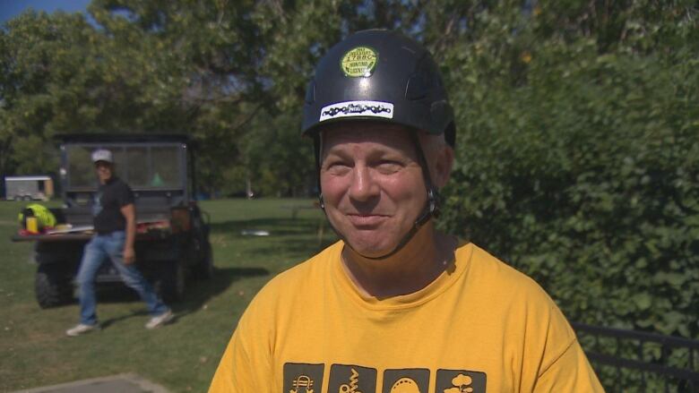 A man stands in front of shrubs in park with helmet on