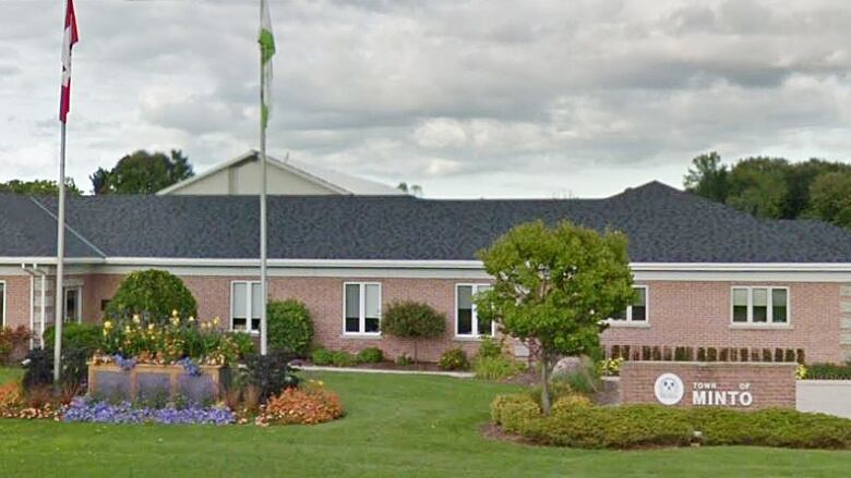 A brick building is seen behind a sign that says 