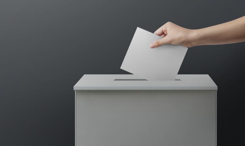 Hand reached out to put white paper into a white ballot box.