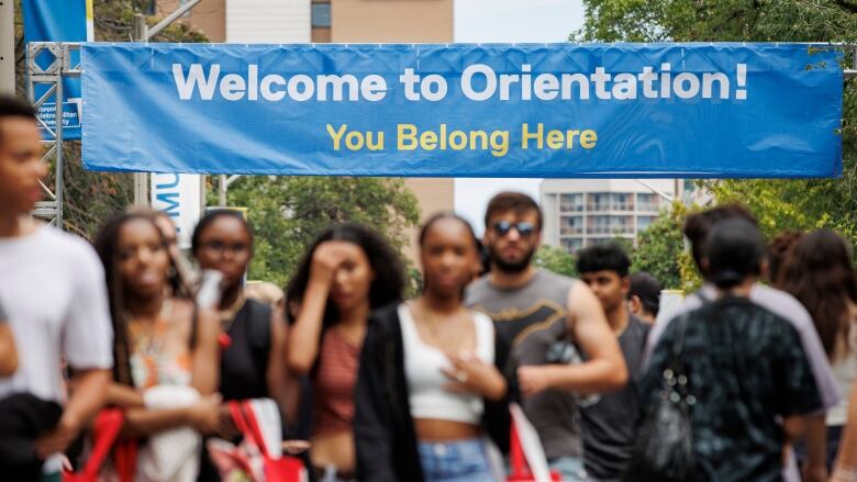 University students walk beneath a large blue sign bearing the message: Welcome to Orientation! You belong here