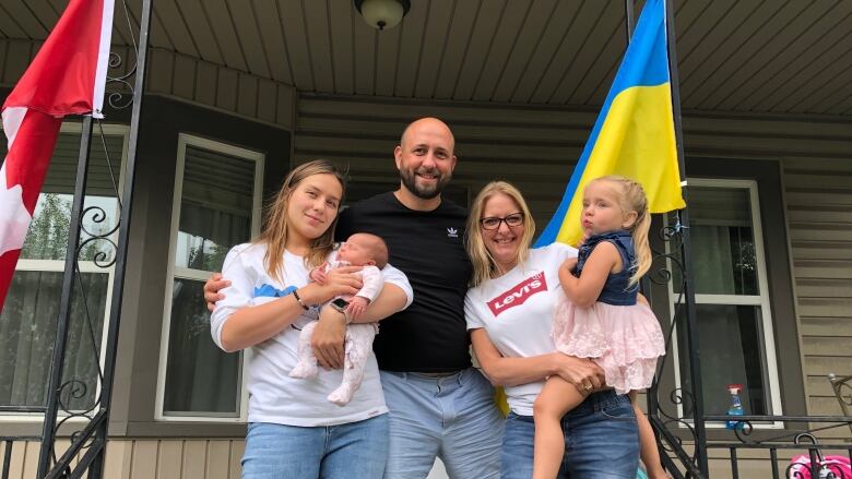 A husband and wife holding their two young daughters with a woman they consider family