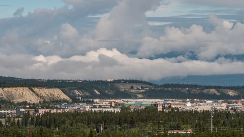 Fluffy clouds over a ridge, urban buildings and a mass of trees. 