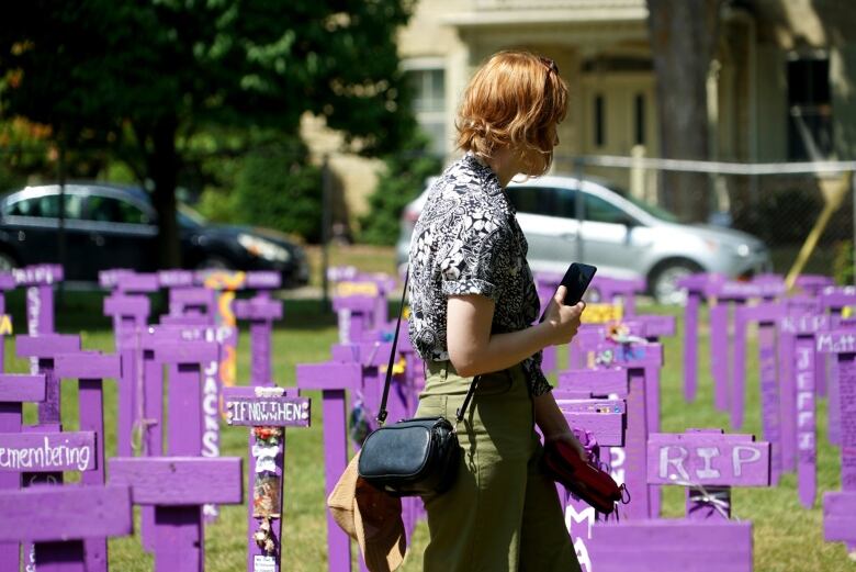 A young woman walks by purple wooden markers in a field. 