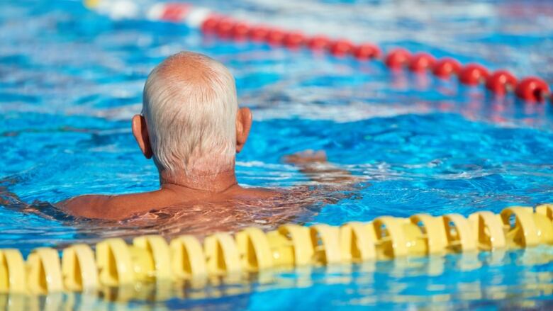 A white-haired man swimming in an outdoor swimming pool.