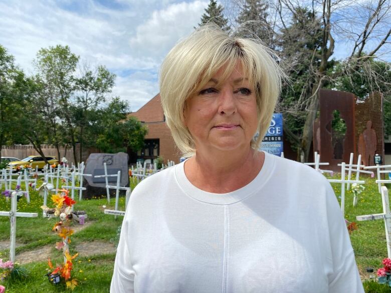 A woman stands outside with white crosses in the background.