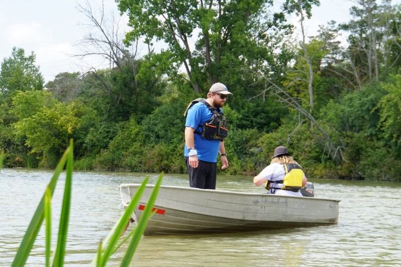 Man in boat on Welland River in lifejacket stares at shoreline, looking for the invasive European water chestnut