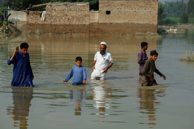 Two men and three boys wade through floodwaters. 