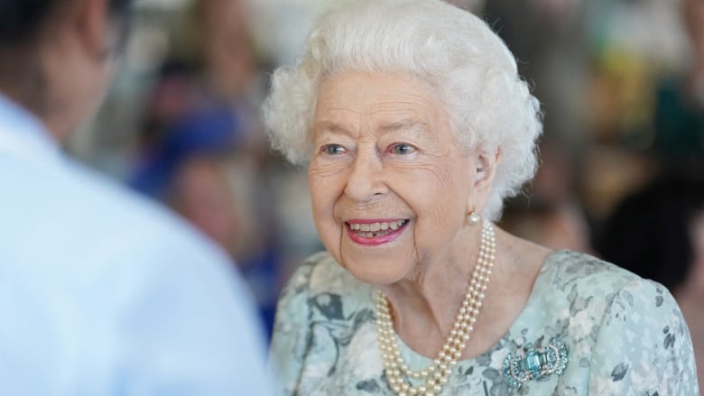 A smiling white-haired woman wearing pearls and a floral dress. 