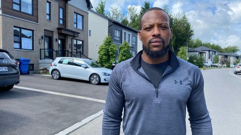 A man stands in front of a parked car outside a home in a suburb. 