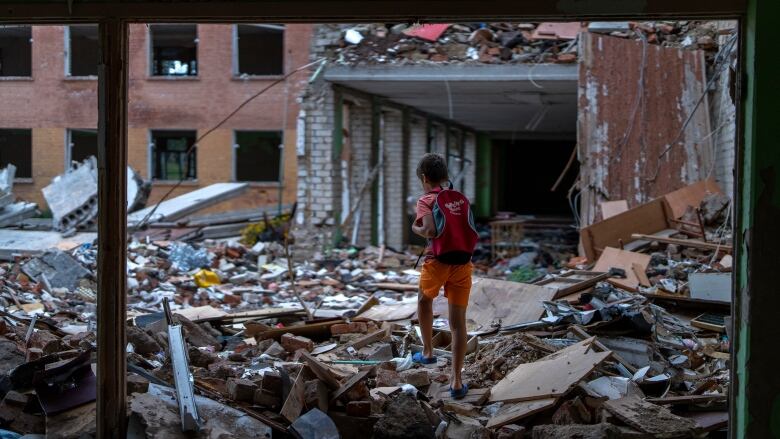 A child wearing a backpack steps through the bombed-out remains of a building.