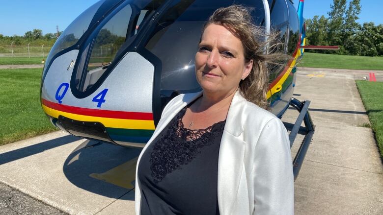 A woman stands in front of a helicopter.