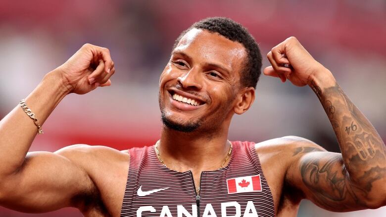 a closeup of Andre De Grasse wearing his Canada jersey raising his hands in celebration and smiling after finishing first in the Men's 200m Semi Final at the Tokyo 2020 Olympic Games