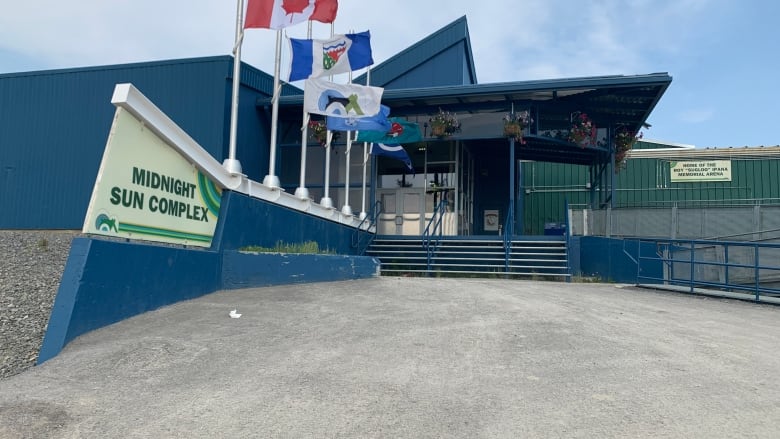 A dusty, dark blue building with flags and a sign. 