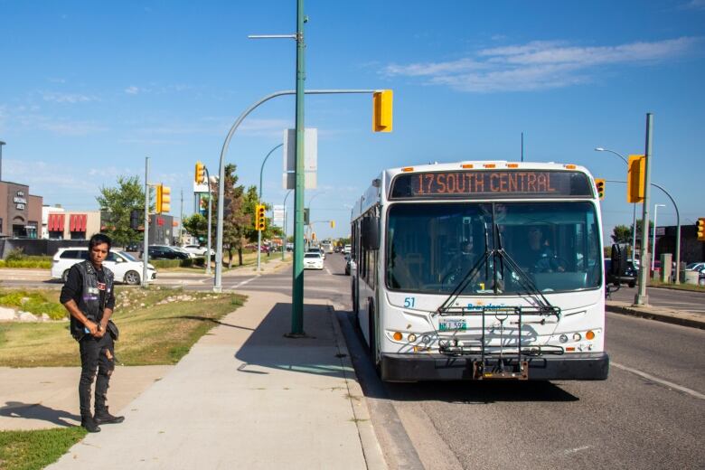 A man stands on the sidewalk waiting for the bus.