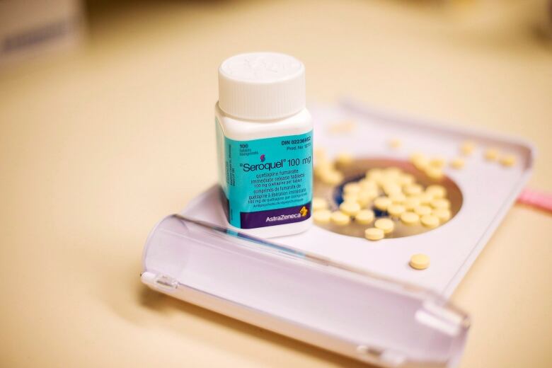 A bottle of pills on a plastic tray in front of several loose pills.