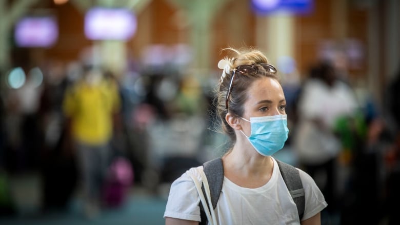 A woman with a blue facemask stands among travellers in an airport.