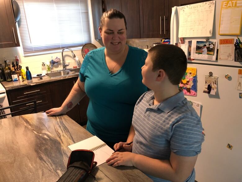 A woman smiles at a boy who is seated at a kitchen island 